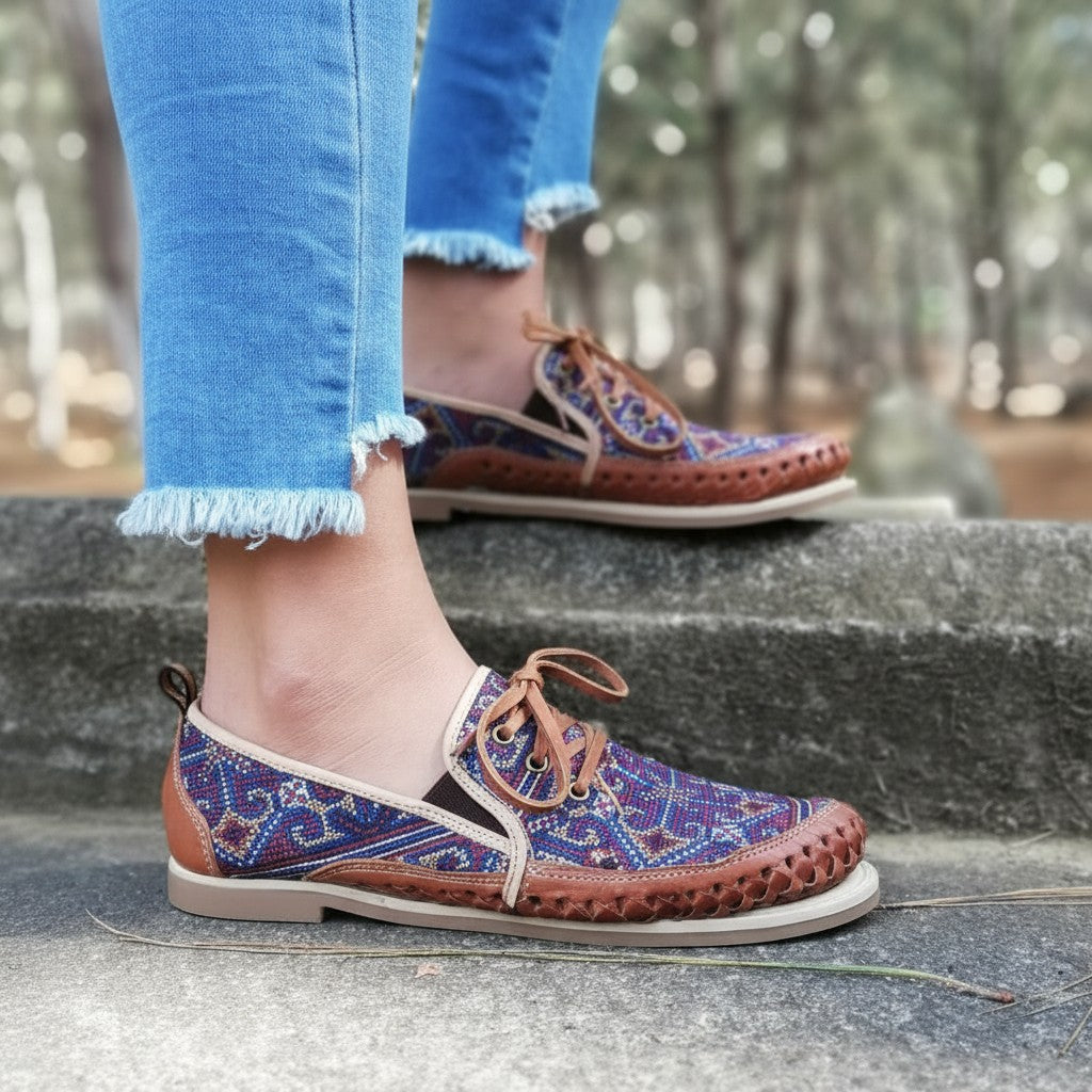 ARTESANALRENVAL women's slip-on shoes with vibrant geometric textile embroidery in blue, terracotta, orange, and white, featuring brown leather trim and a low profile sole.