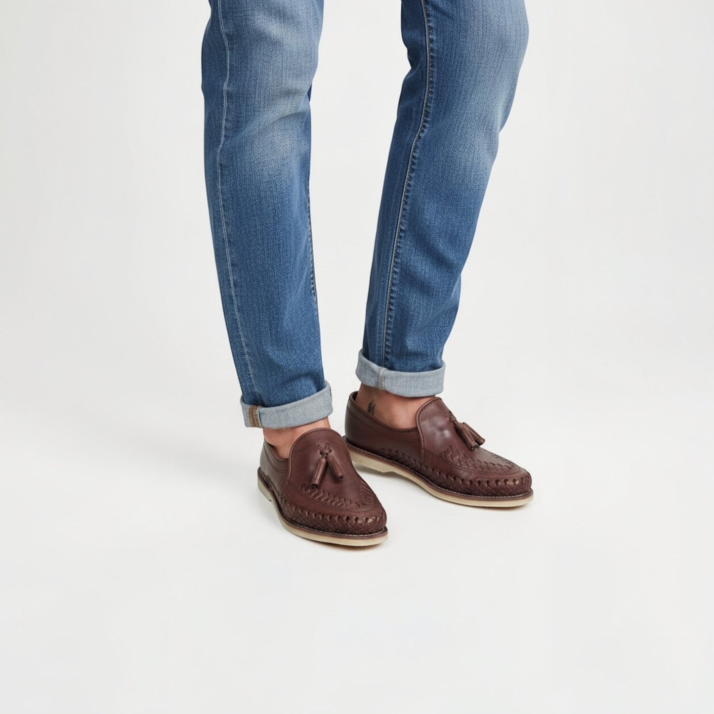 Mocasines ARTESANALRENVAL de piel marrón chocolate con trenzado artesanal y borlas, combinados con vaqueros azules.