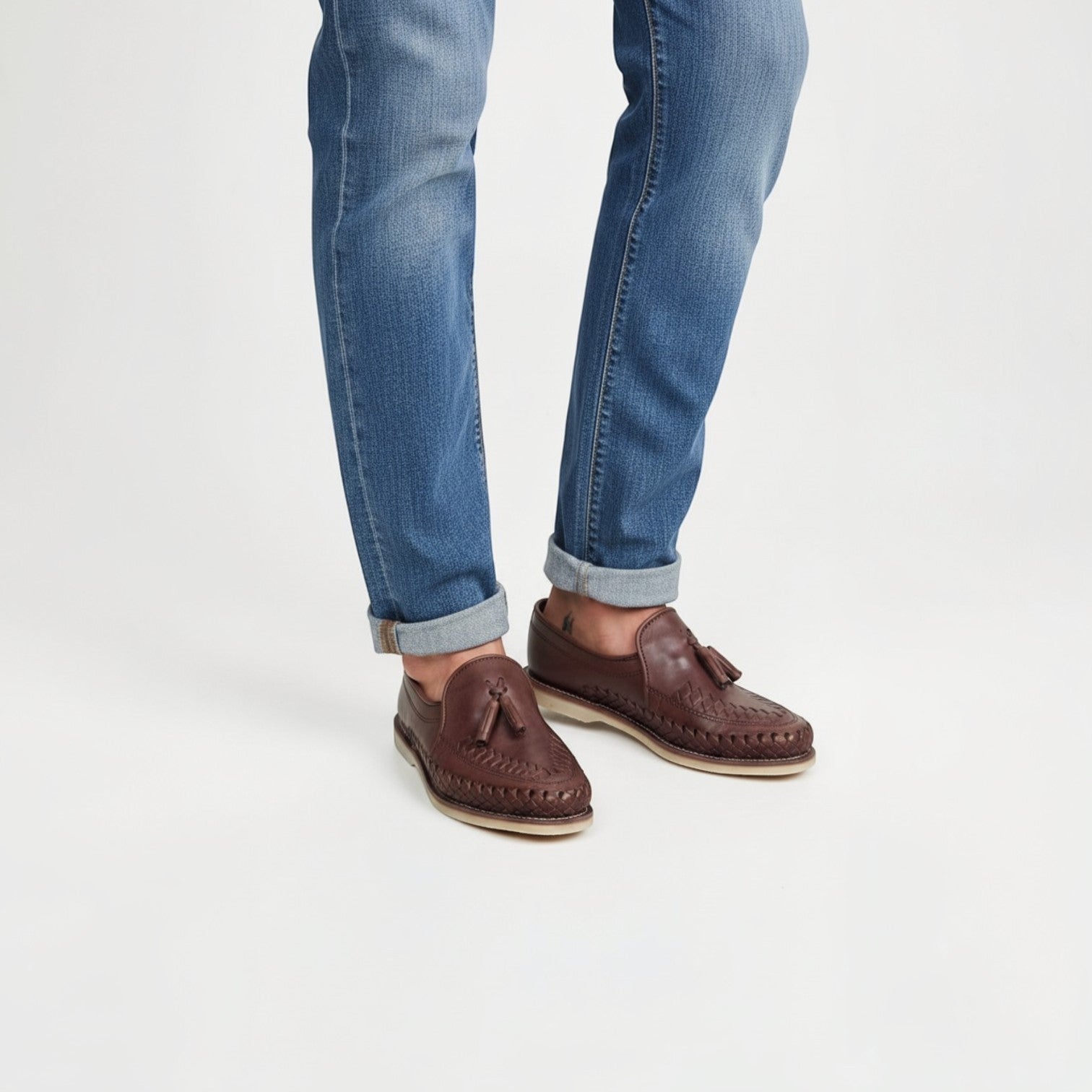 Mocasines ARTESANALRENVAL de piel marrón chocolate con trenzado artesanal y borlas, combinados con vaqueros azules.