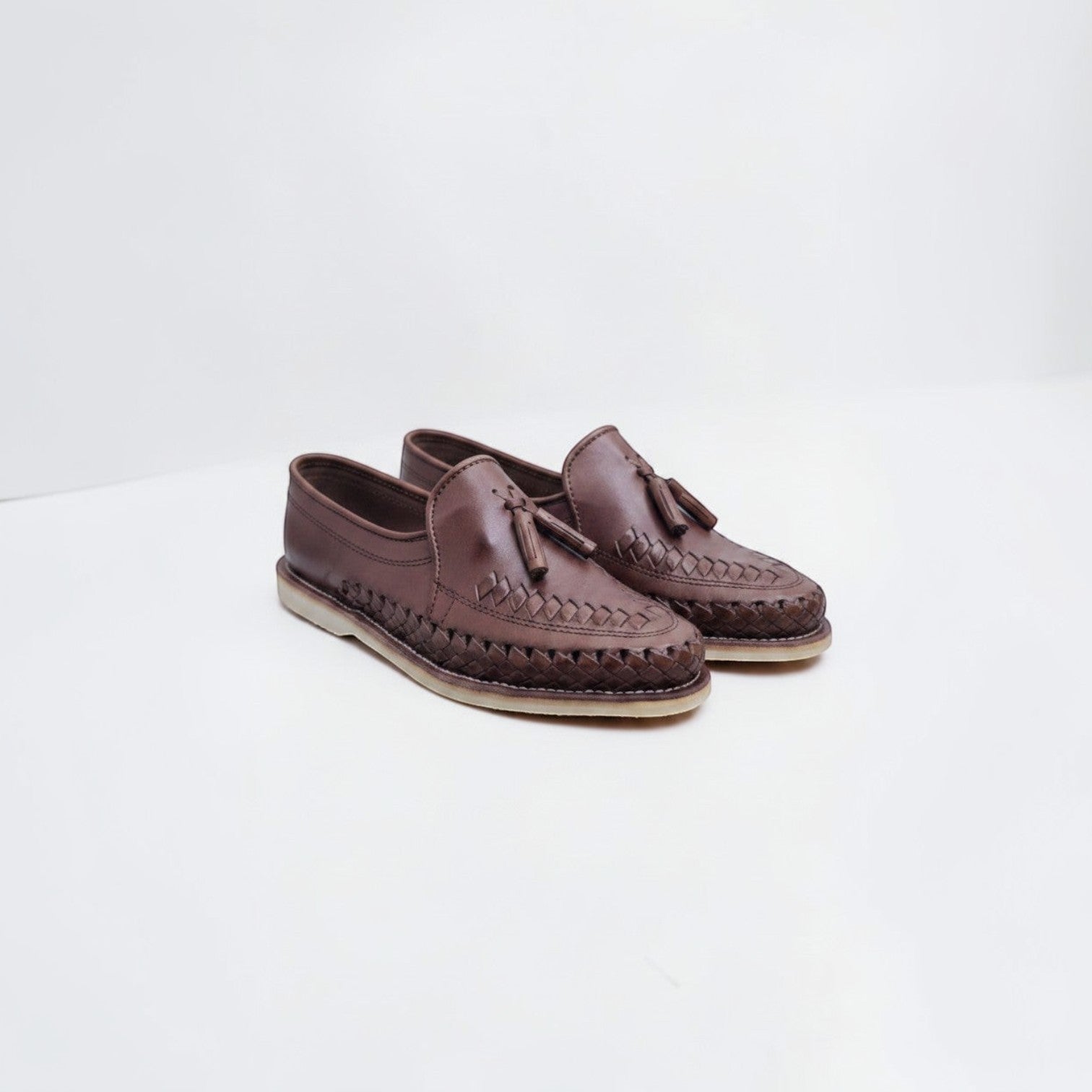 Mocasines ARTESANALRENVAL de piel marrón chocolate con trenzado artesanal y borlas decorativas en el empeine.